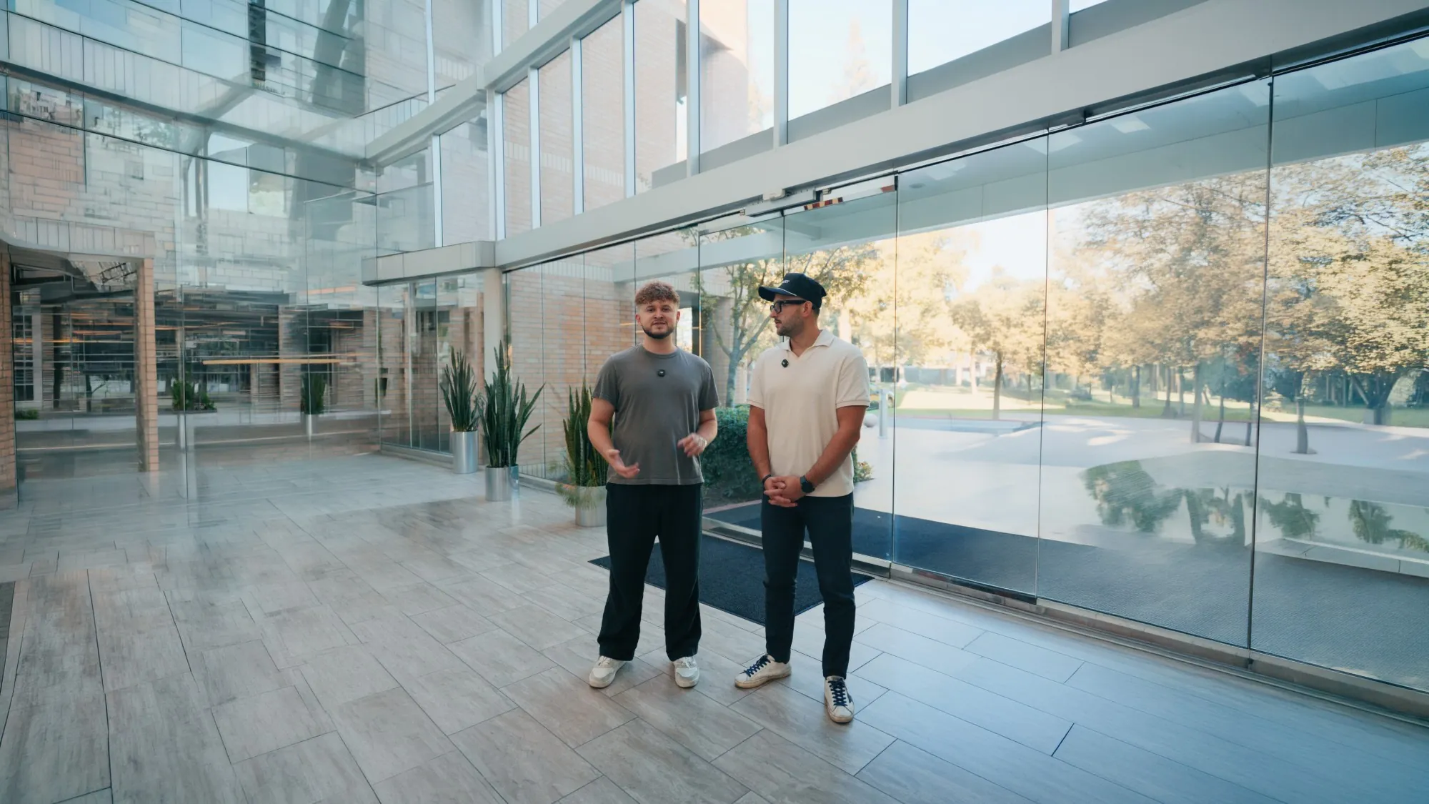 Two men talking to camera in a bright glass office lobby
